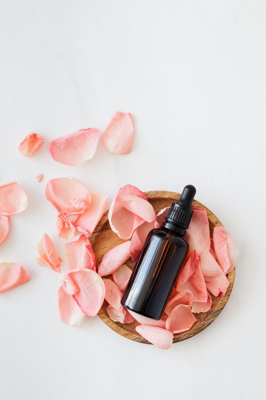 Rose petals with essence flask on wooden plate